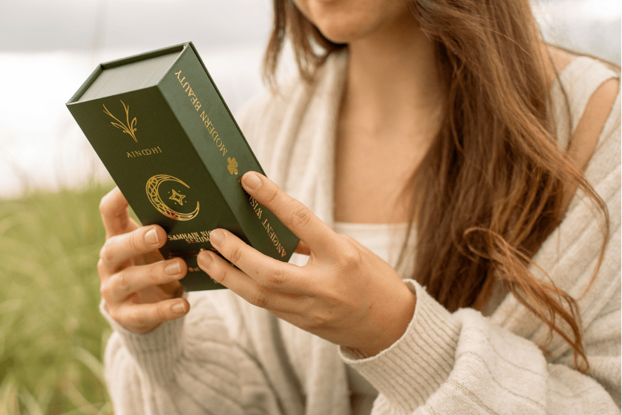 A woman holding the green and gold outer box of award-winning AINMHÍ samhain night serum